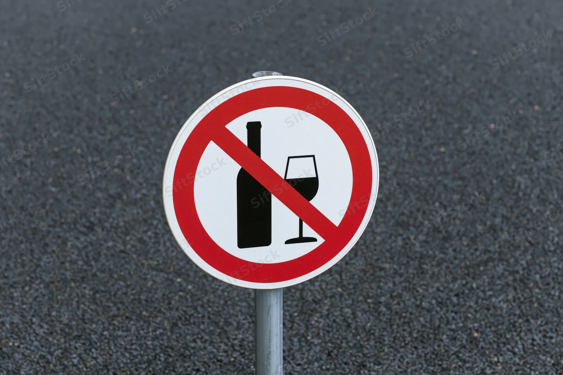 Round prohibition sign with crossed-out bottle and wineglass on metal pole against asphalt road surface