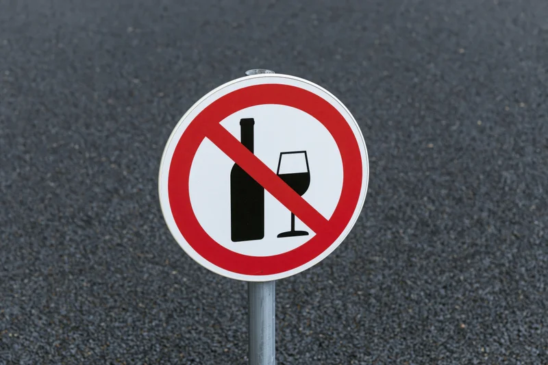 Round prohibition sign with crossed-out bottle and wineglass on metal pole against asphalt road surface