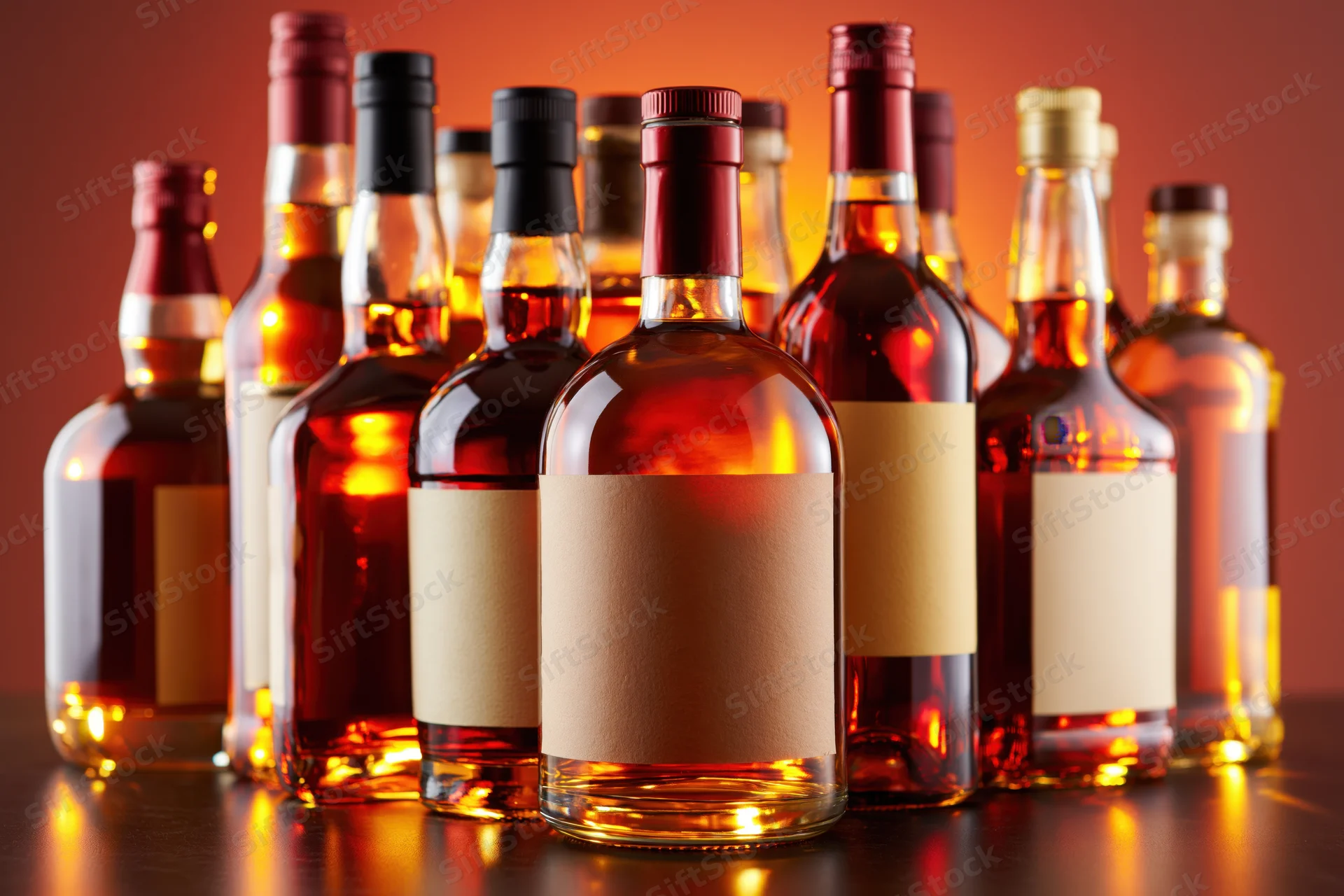 Assorted whiskey and bourbon bottles with blank labels arranged in a row on a dark surface under warm lighting