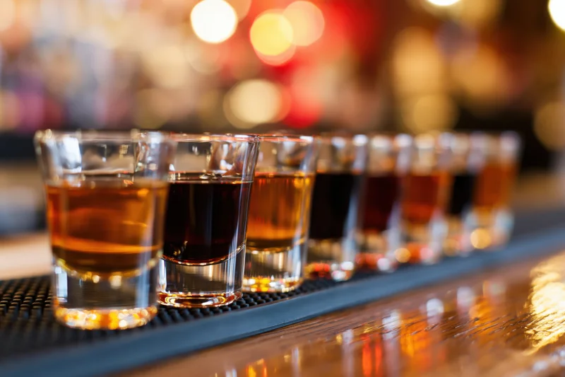 Row of shot glasses filled with amber and dark brown liquor lined on a bar counter