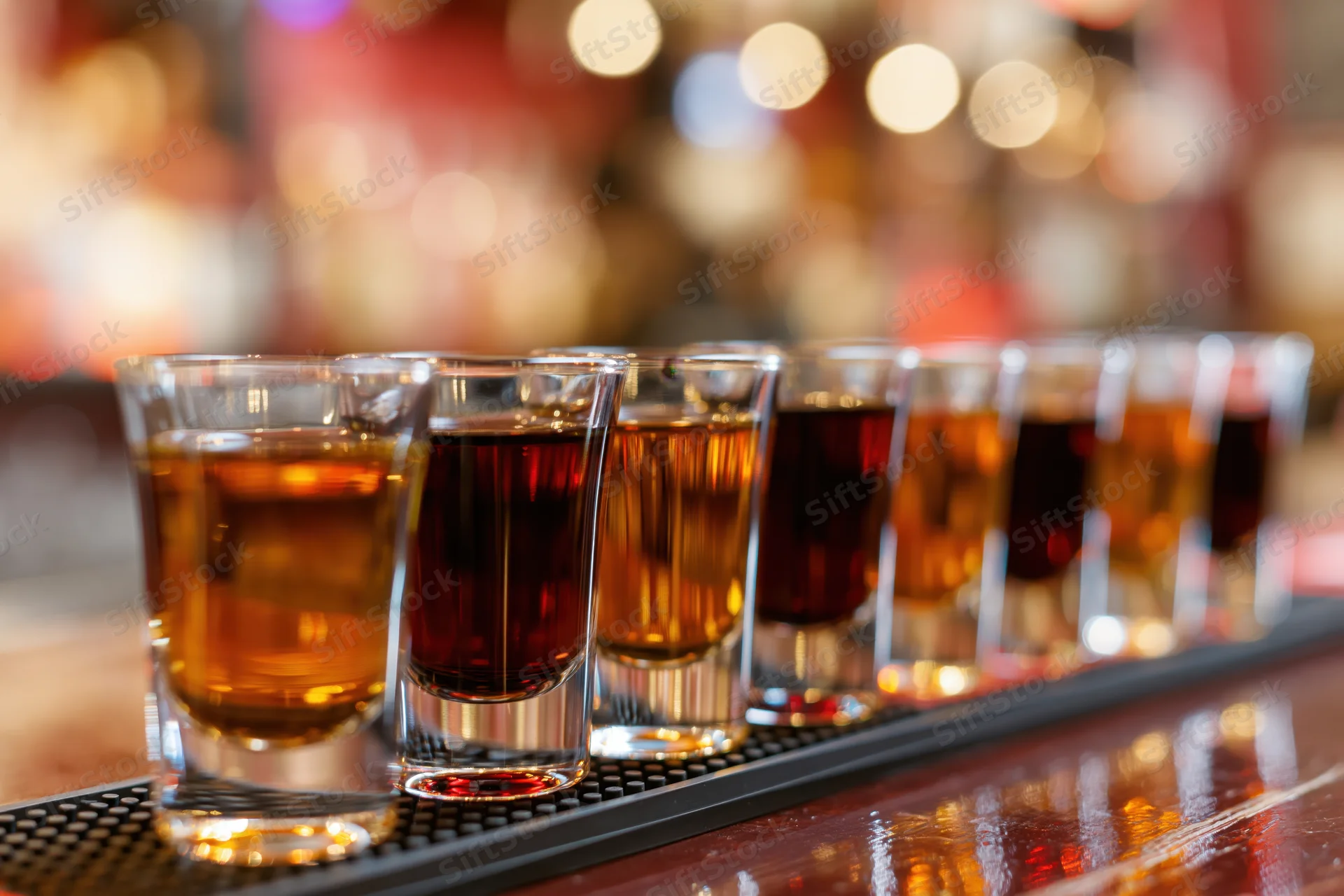Row of shot glasses filled with amber and dark brown liquor on a bar mat
