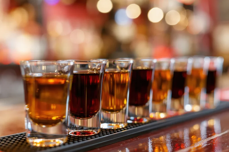 Row of shot glasses filled with amber and dark brown liquor on a bar mat