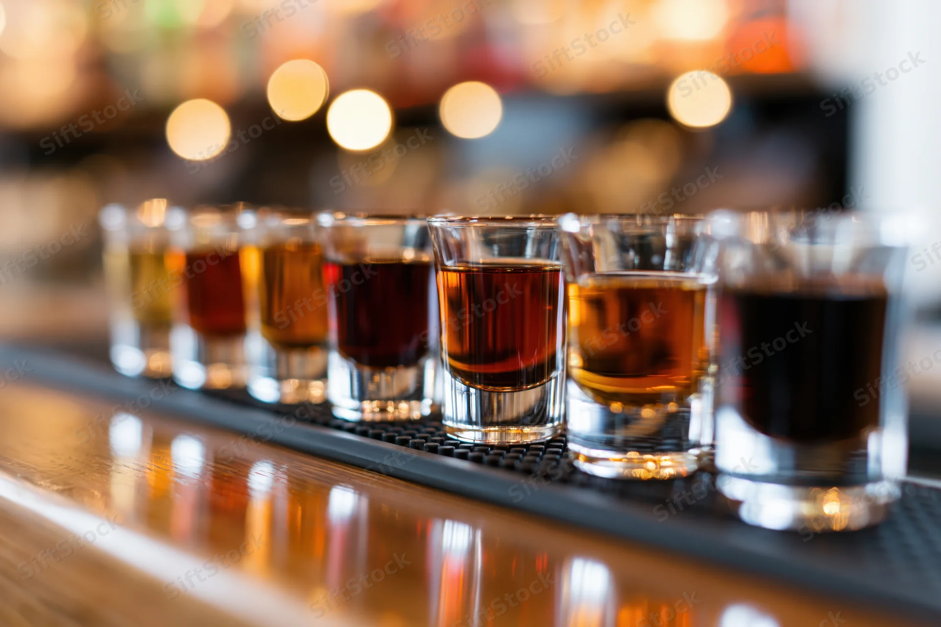 Row of shot glasses filled with amber and dark brown liquor on a bar counter