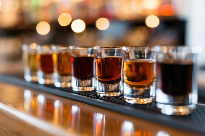 Row of shot glasses filled with amber and dark brown liquor on a bar counter