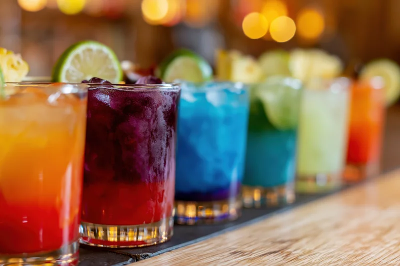 Row of colorful cocktails with lime garnishes on a bar counter