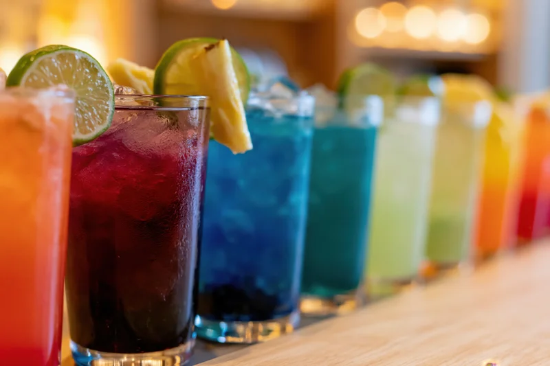 Row of colorful cocktails with lime and pineapple garnishes on a bar counter