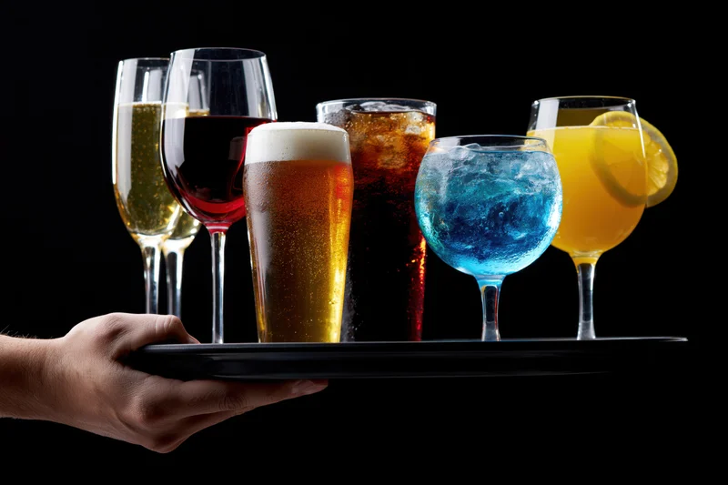 Hand holding a tray with assorted drinks against a black background