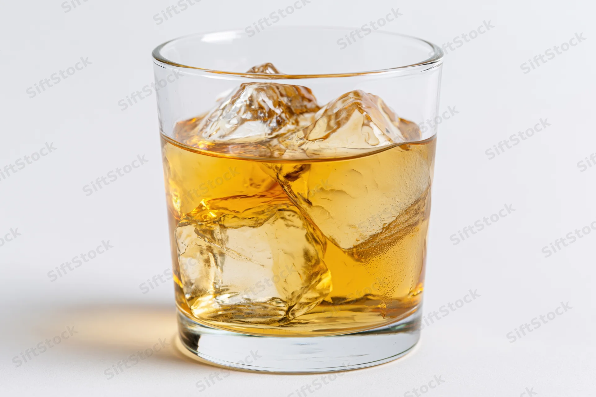 Amber whiskey with ice cubes in a short glass on white surface