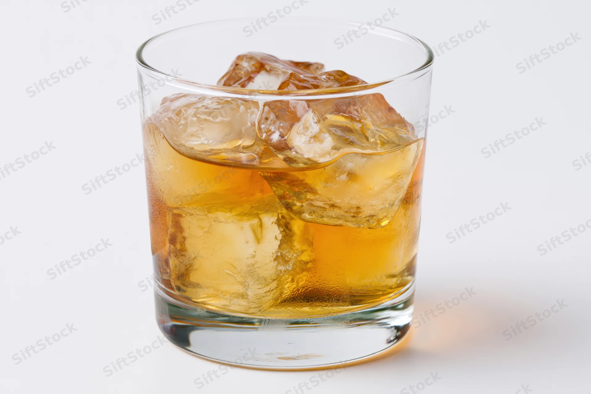 Amber whiskey with ice cubes in a clear rocks glass on white background