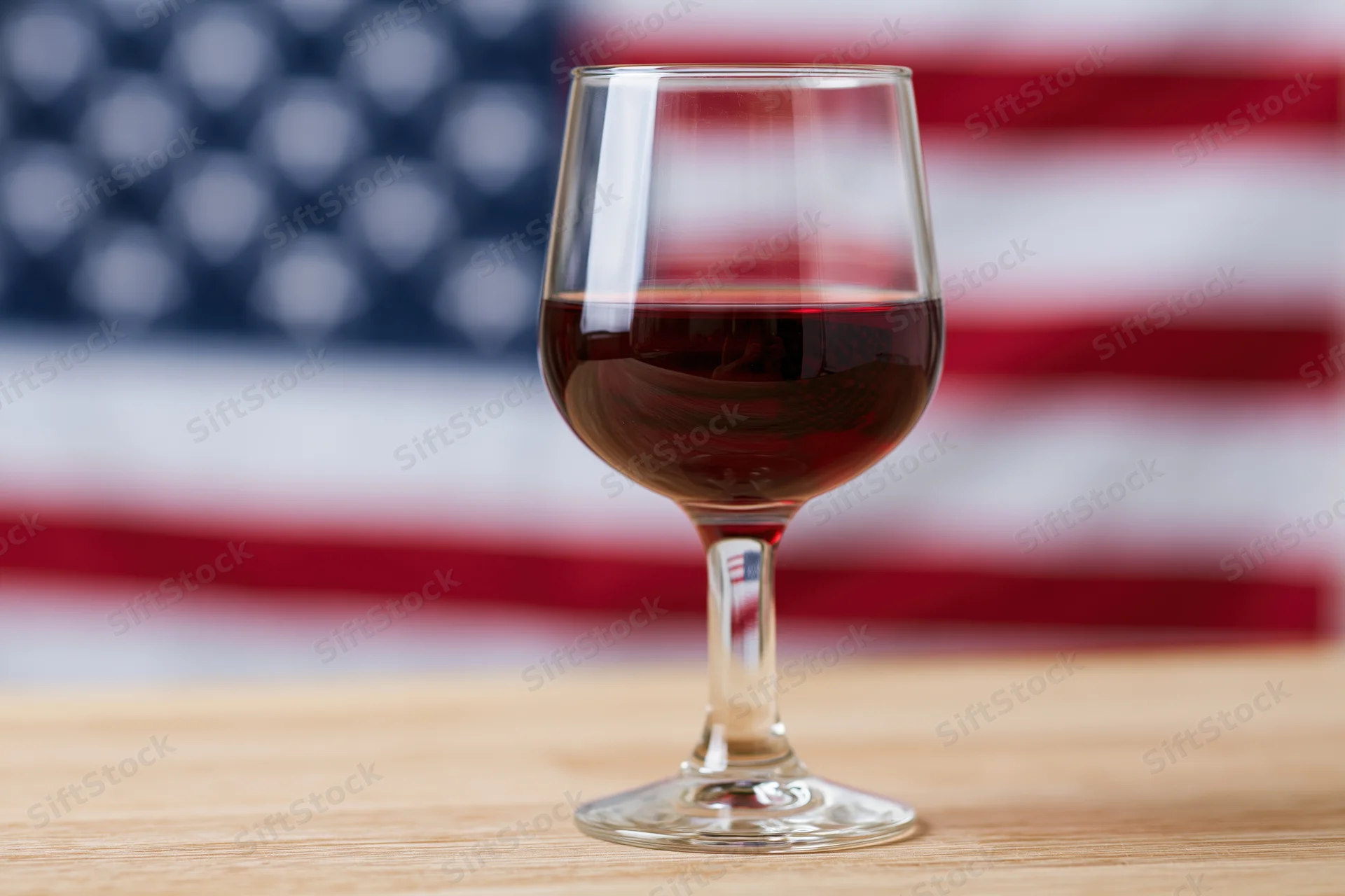 Wine glass filled with red wine on wooden table with blurred american flag in background