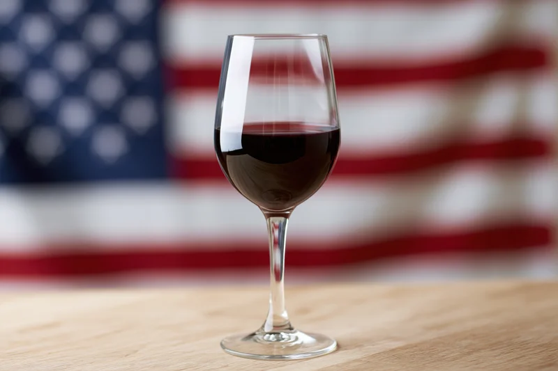 Wine glass filled with red wine on wooden table with american flag in background