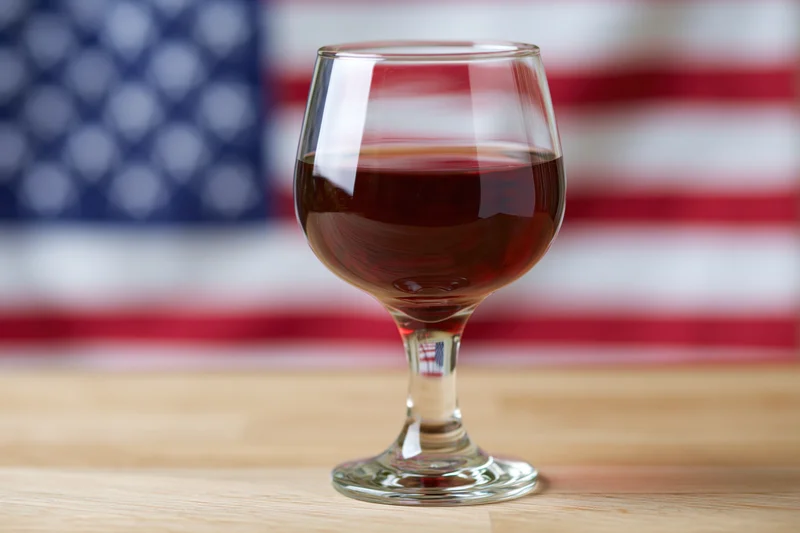 Wine glass filled with red wine on wooden table with american flag in blurred background