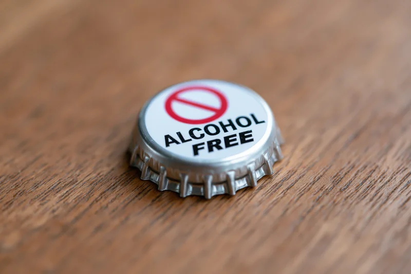 Metal bottle cap with alcohol free label and prohibition symbol on wooden surface