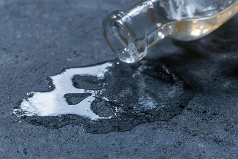 Glass bottle spilling liquid onto pavement forming skull shape