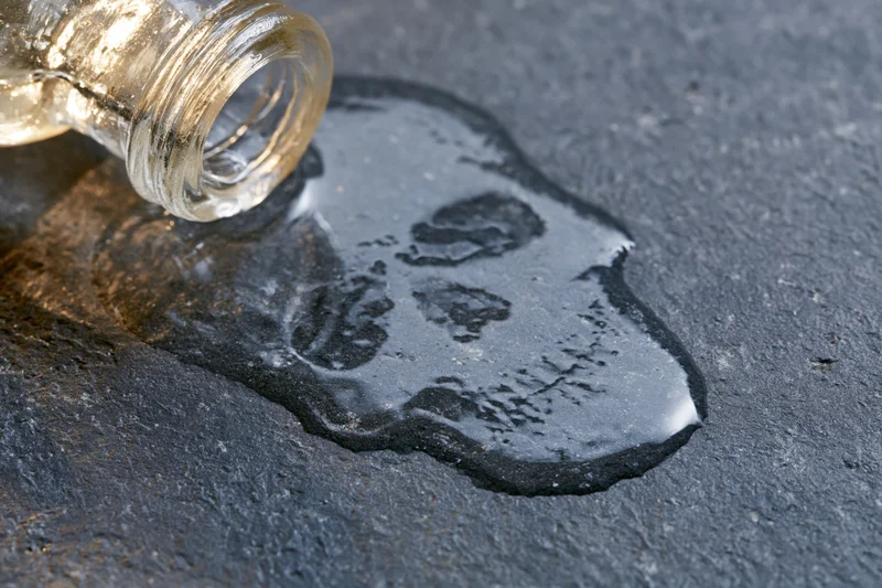 Glass bottle tipped over spilling liquid onto dark pavement surface
