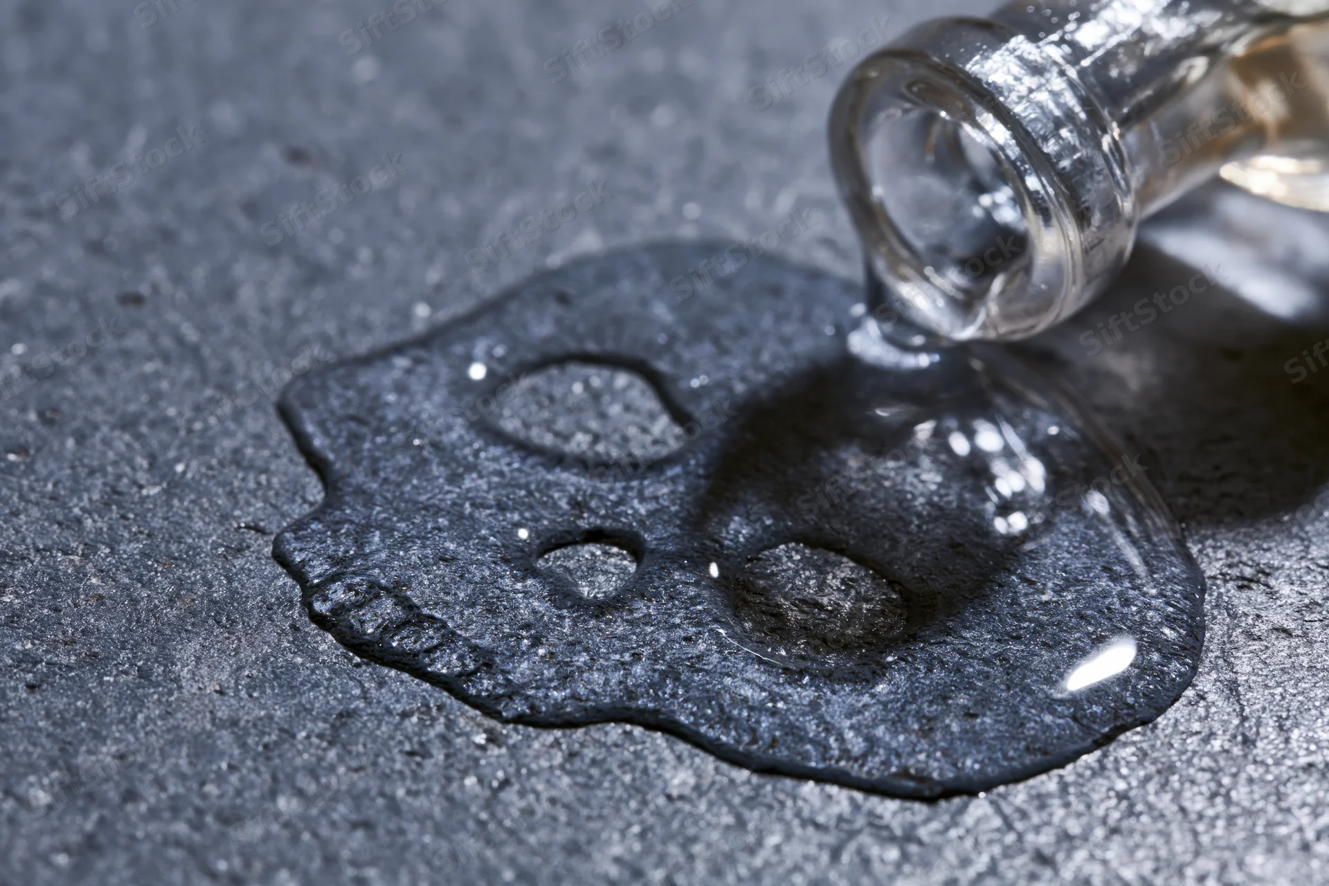 Liquid spilling from a glass bottle forming a skull shape on a dark textured surface