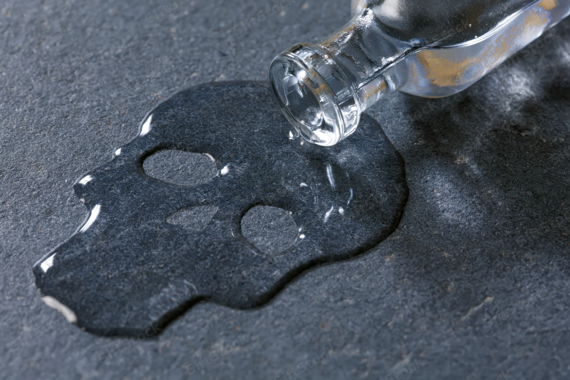 Spilled liquid forming skull shape on dark surface beside glass bottle