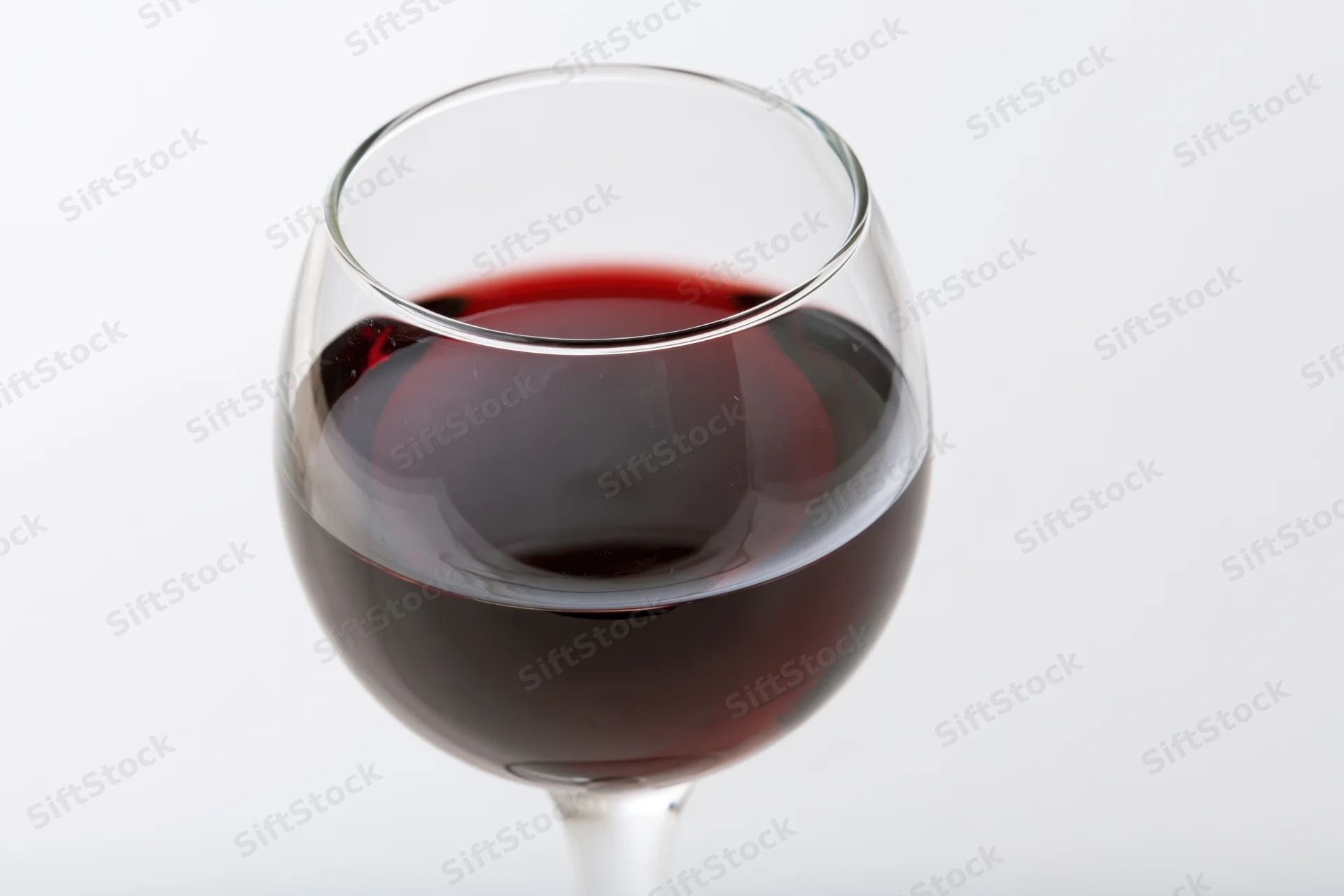 Stemmed wine glass half-filled with deep red wine centered on white background