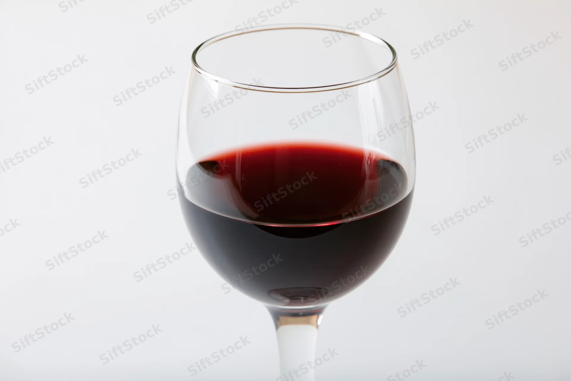 Stemmed wine glass half-filled with deep red wine centered on white background