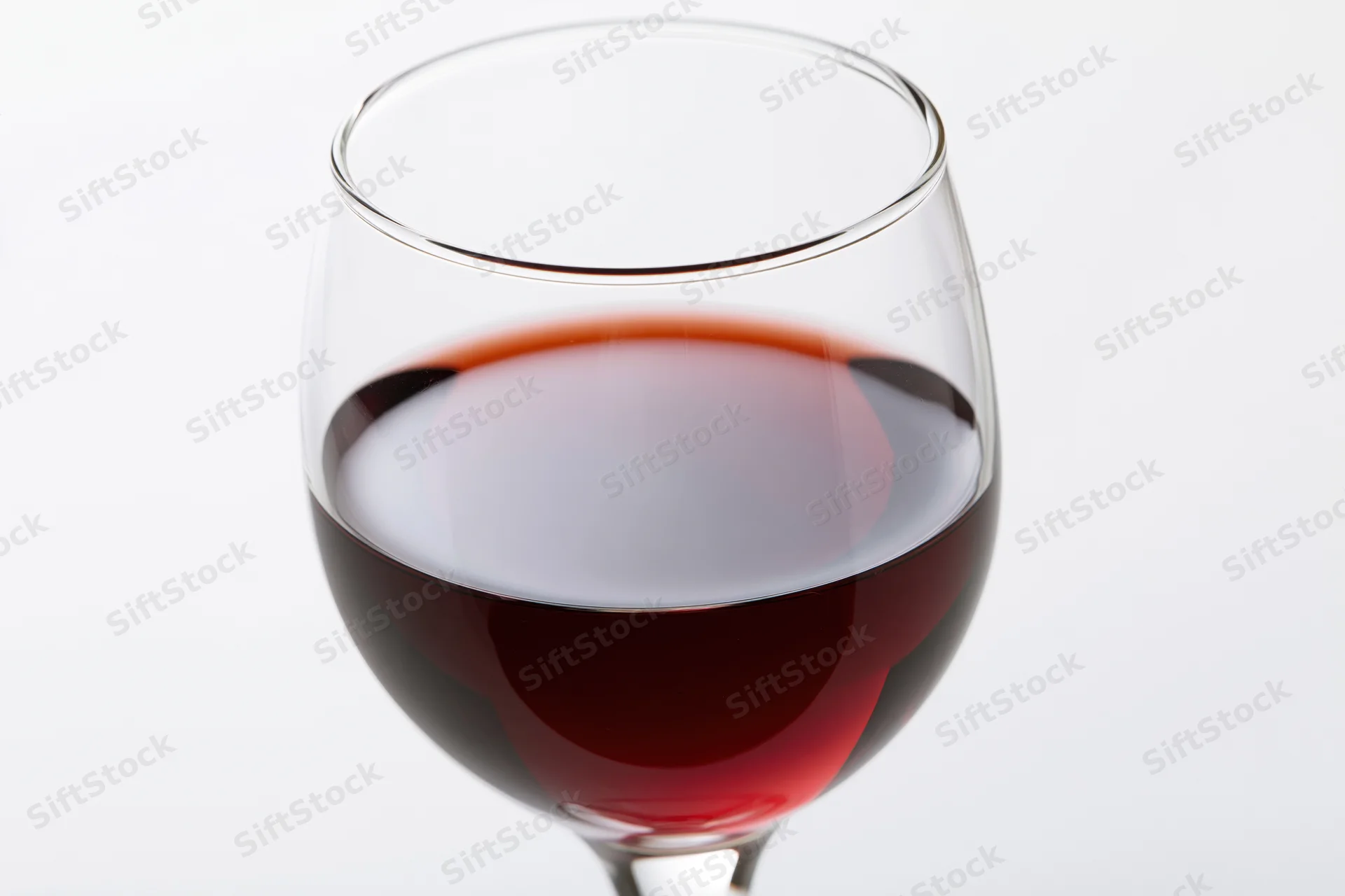 Stemmed wine glass half-filled with deep red wine centered on white background
