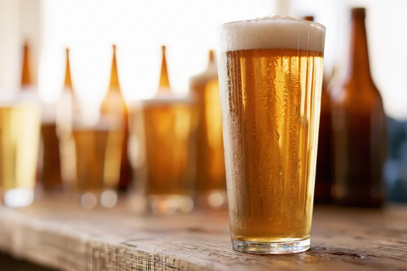 Tall pint glass filled with golden lager and foamy head on wooden bar surface