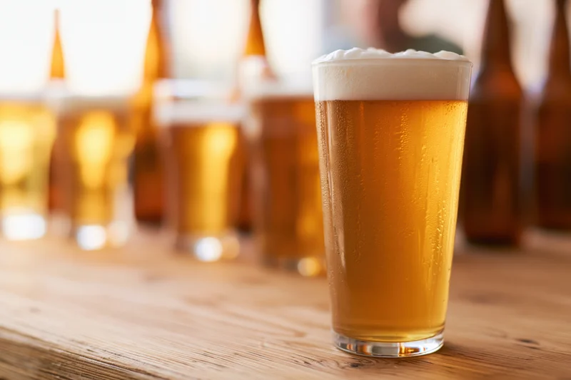 Tall pint glass filled with golden lager and foamy head on wooden table