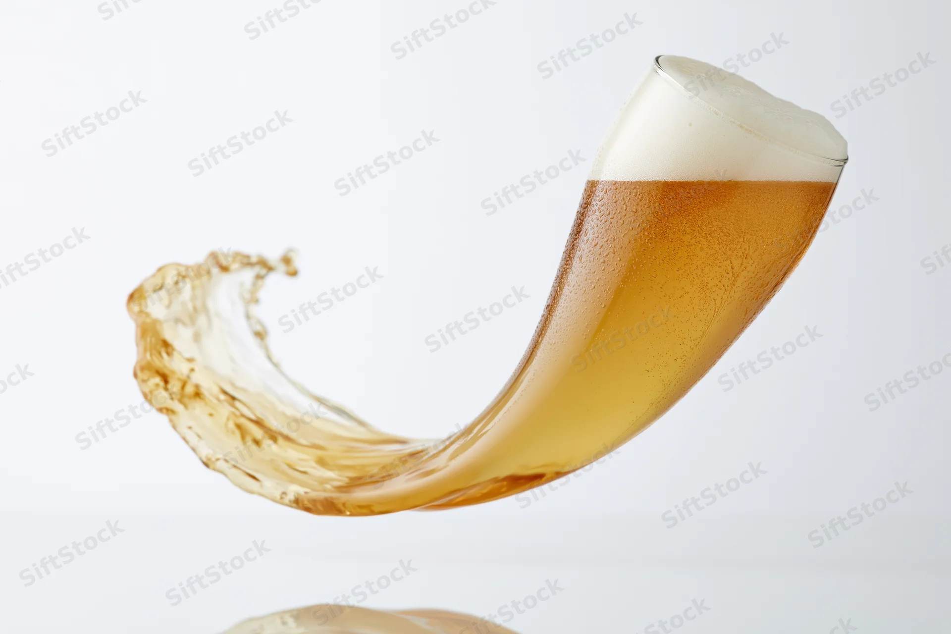 A tilting glass of lager splashing beer liquid in motion against a white background