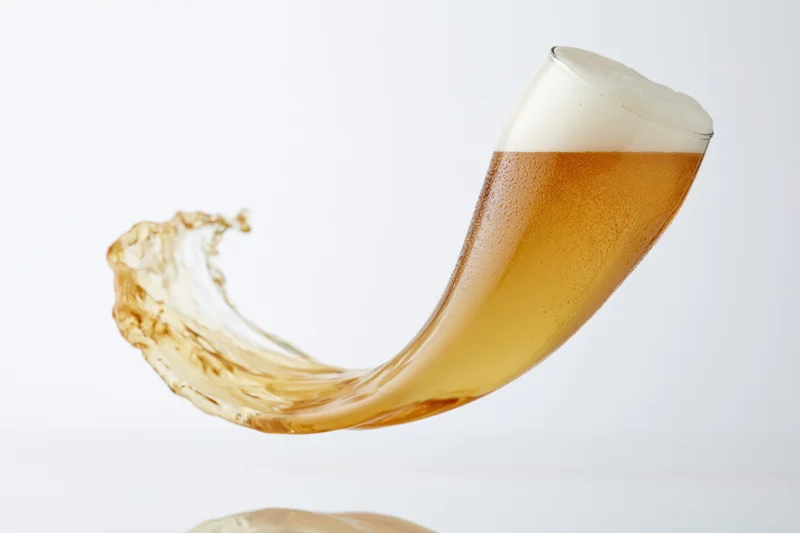 A tilting glass of lager splashing beer liquid in motion against a white background