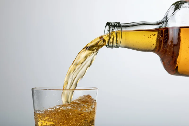 Amber whiskey being poured from a glass bottle into a tumbler with ice