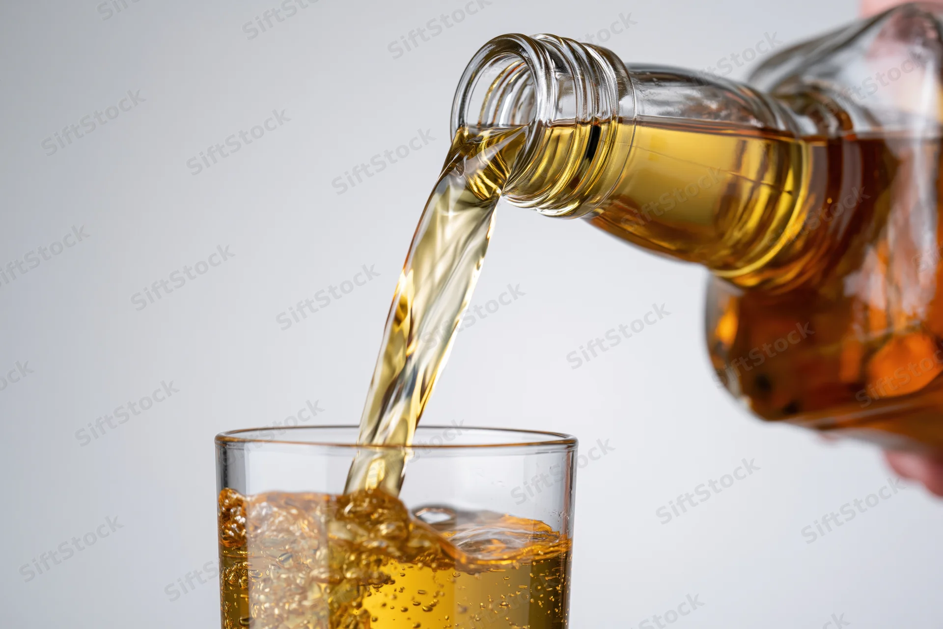 Amber whiskey being poured from a glass bottle into a tumbler with ice