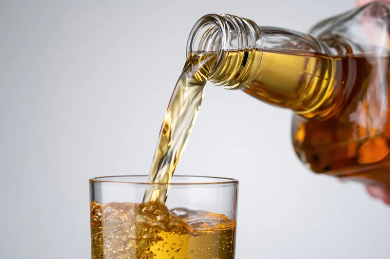 Amber whiskey being poured from a glass bottle into a tumbler with ice