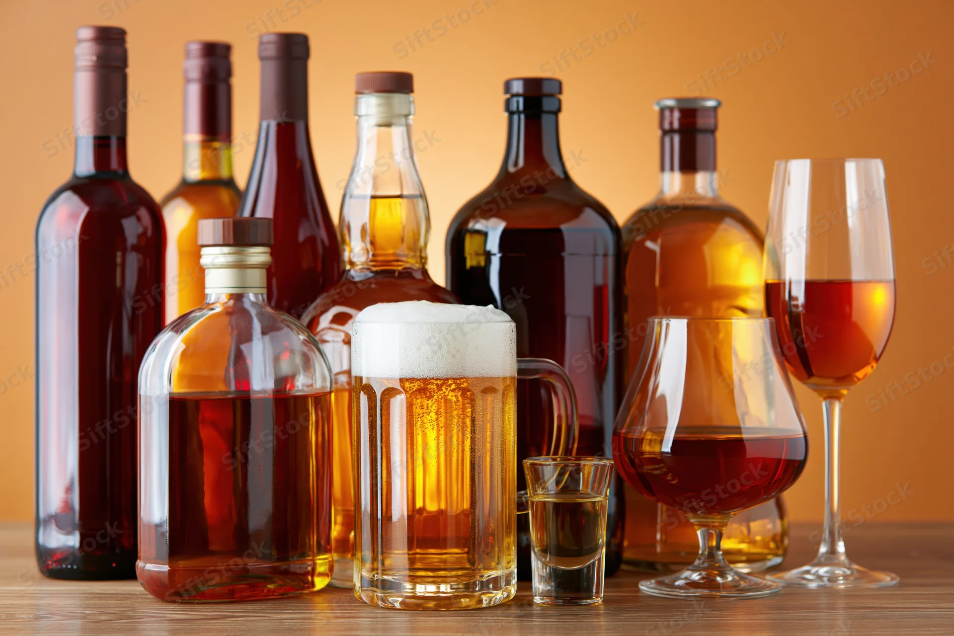 Assorted alcohol bottles and glasses arranged on a wooden table