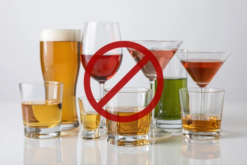 Assorted alcoholic drinks arranged on reflective white surface with red prohibition symbol overlaid
