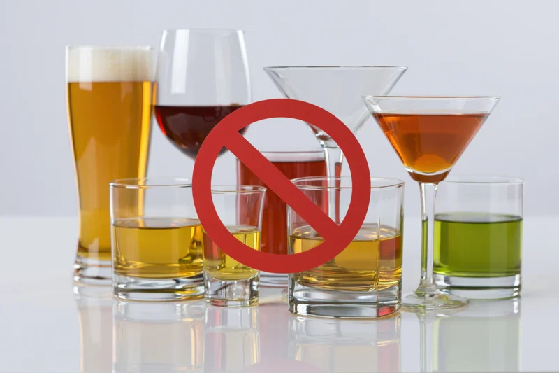 Assorted alcohol drinks arranged with a red prohibition symbol over them on a white reflective surface