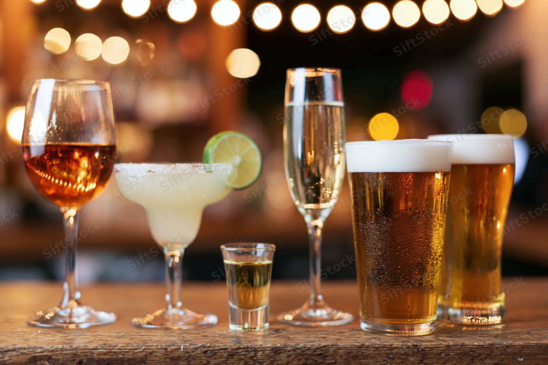Assorted alcoholic drinks lined up on a wooden bar counter under warm ambient lighting