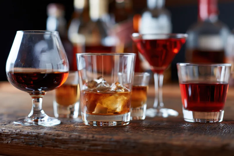 Assorted bar glasses filled with various spirits arranged on a wooden table