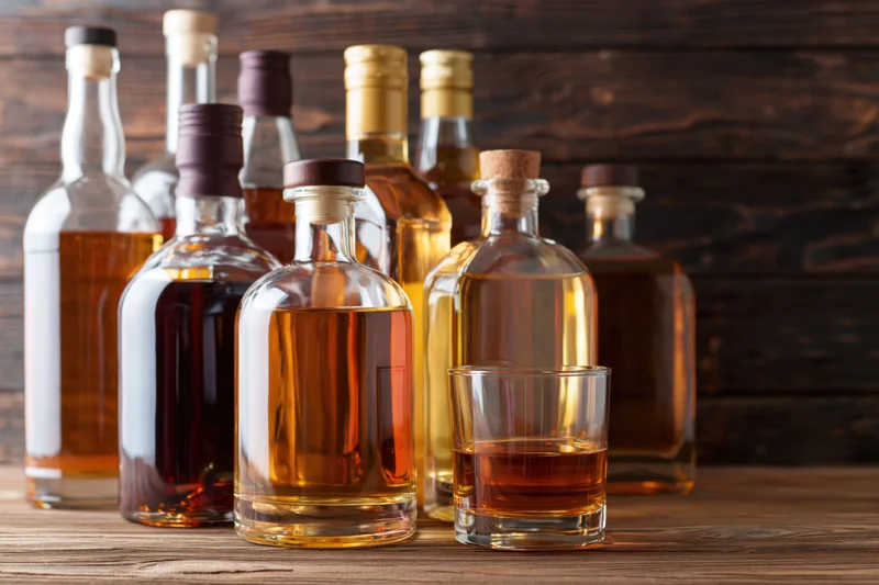 Assorted liquor bottles and a lowball glass of whiskey arranged on a wooden table