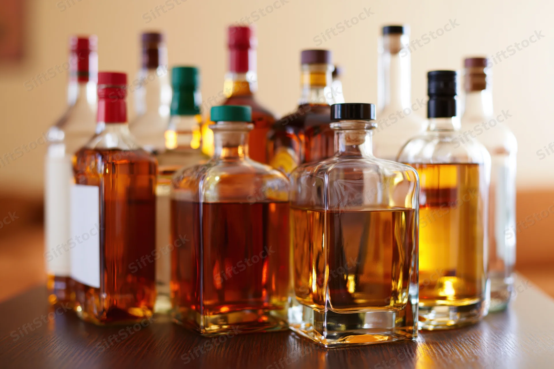 Assorted liquor bottles of varying sizes grouped together on a wooden table indoors