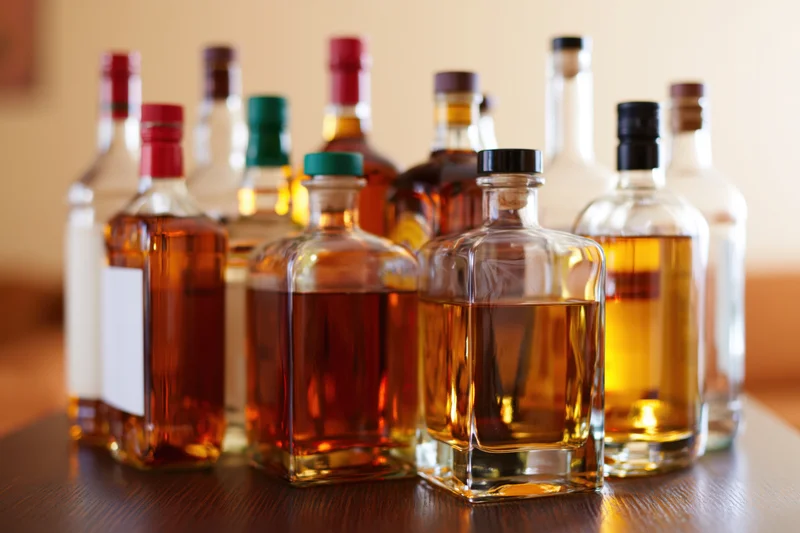 Assorted liquor bottles of varying sizes grouped together on a wooden table indoors