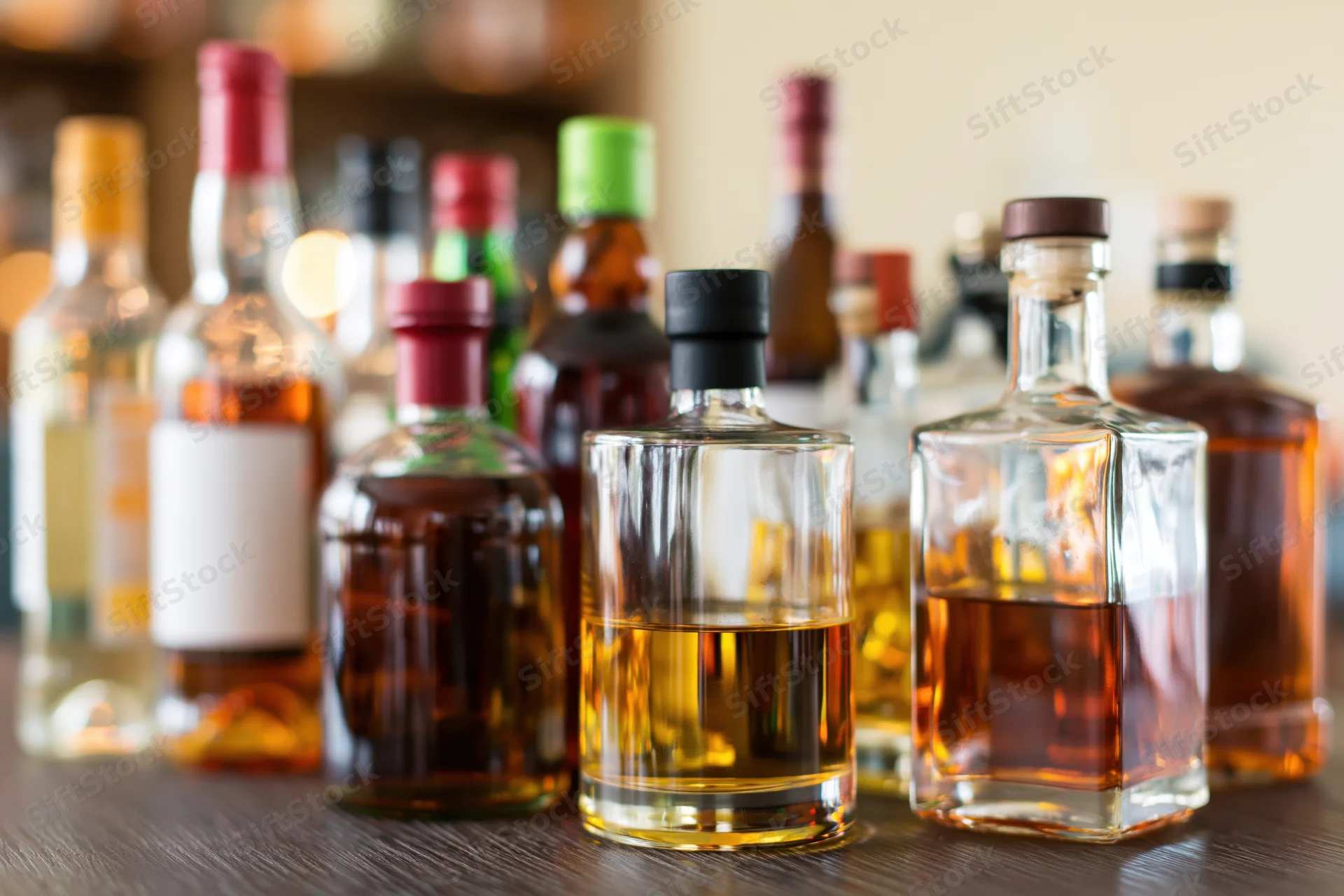 Assorted liquor bottles arranged on a wooden bar countertop with blurred background and copyspace