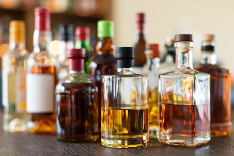 Assorted liquor bottles arranged on a wooden bar countertop with blurred background and copyspace