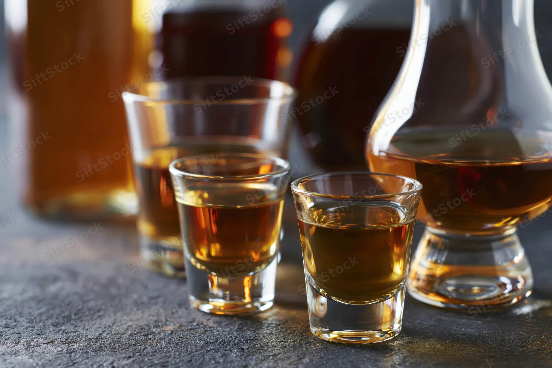 Whiskey and cognac glasses arranged on a dark wet stone surface