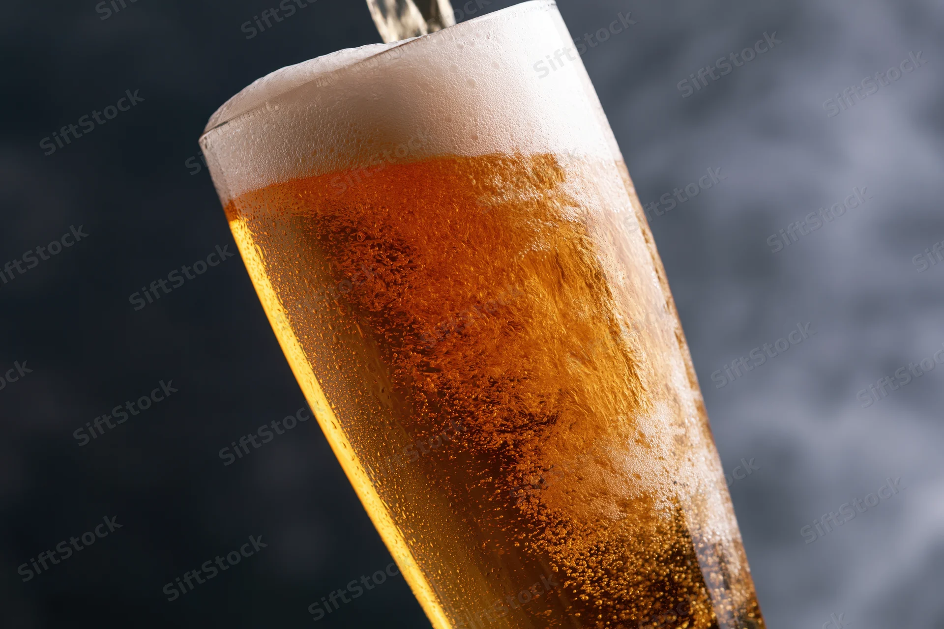 Golden lager being poured into a tall pilsner glass with foam and condensation