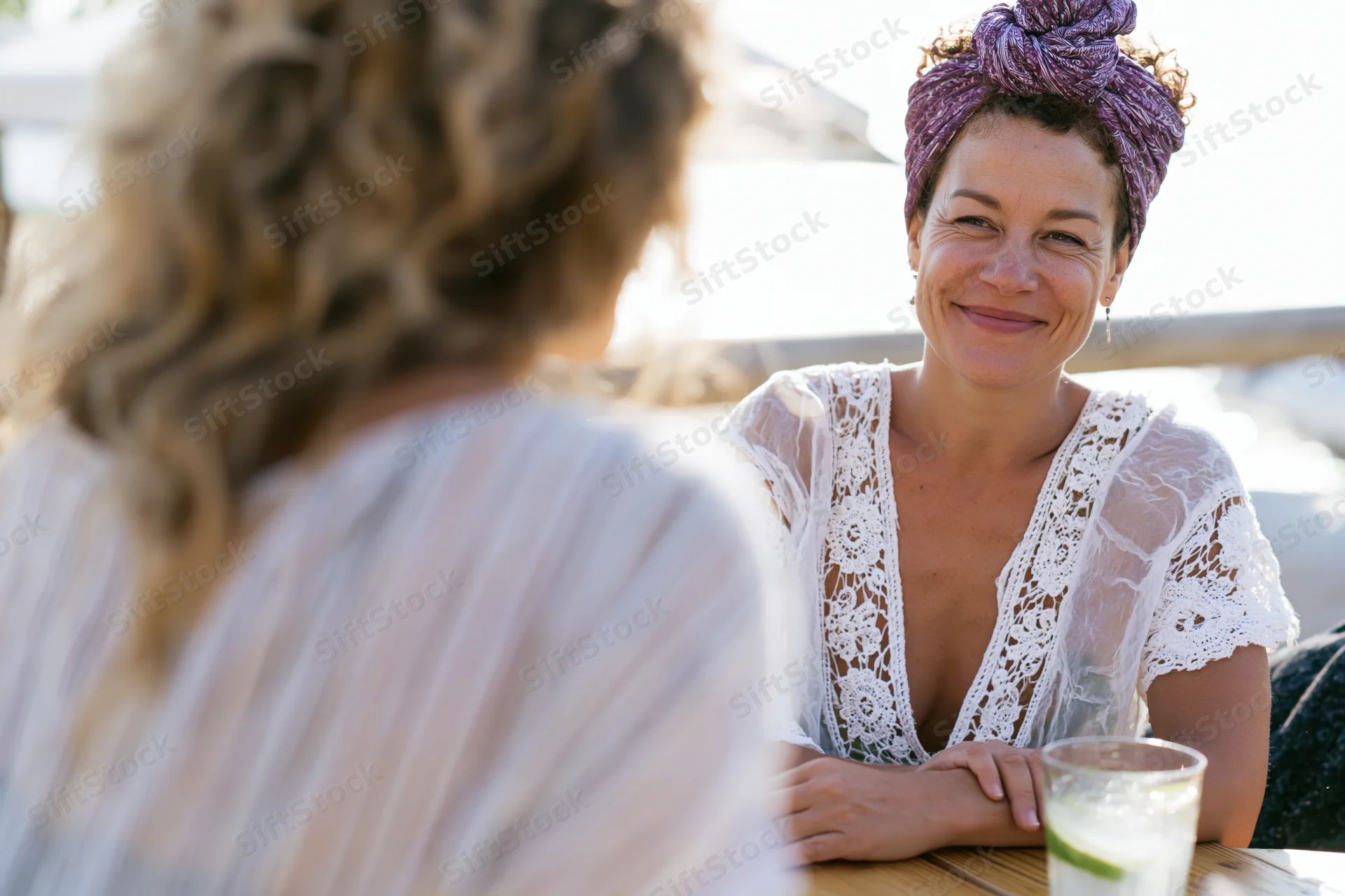 Woman smiling during conversation at outdoor cafe table with drink and lime garnish