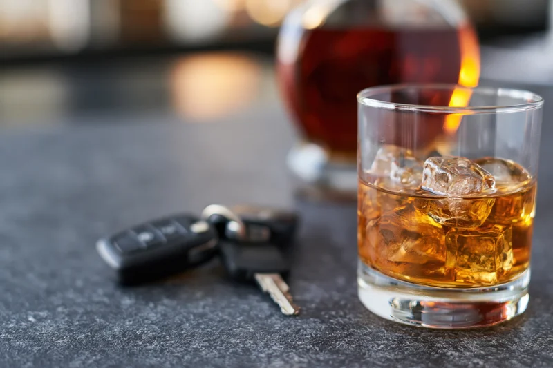 Whiskey glass with ice and car keys on a dark bar surface
