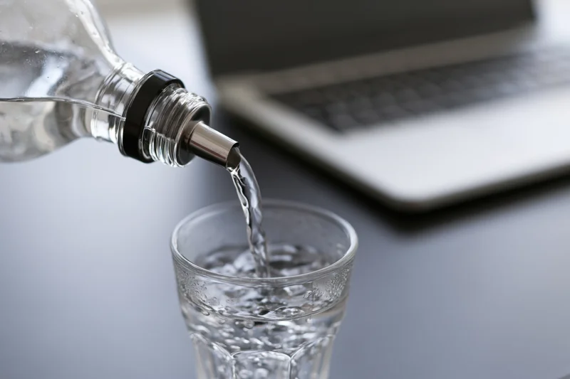 Clear glass bottle with spout tilting to pour water into a glass