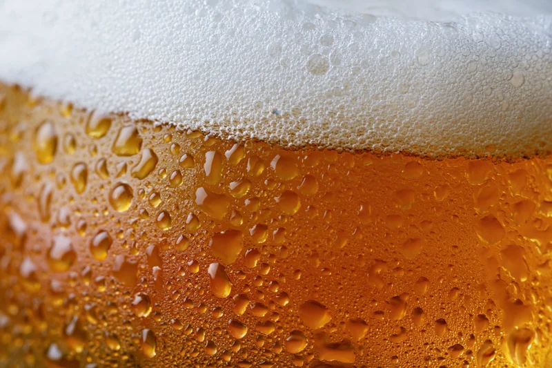 Close-up of condensation droplets on a cold beer glass with white foam head