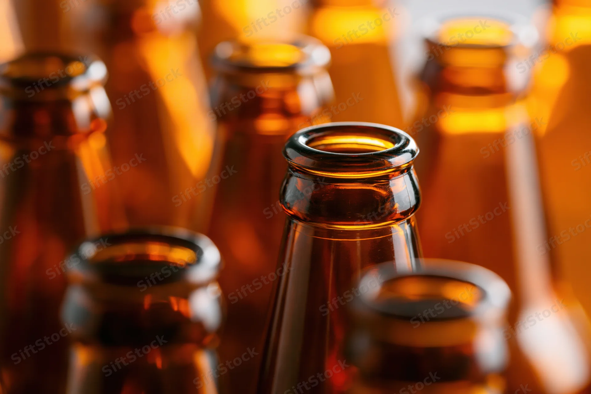 Close-up of empty amber glass beer bottle necks arranged in rows with warm lighting and shallow depth of field