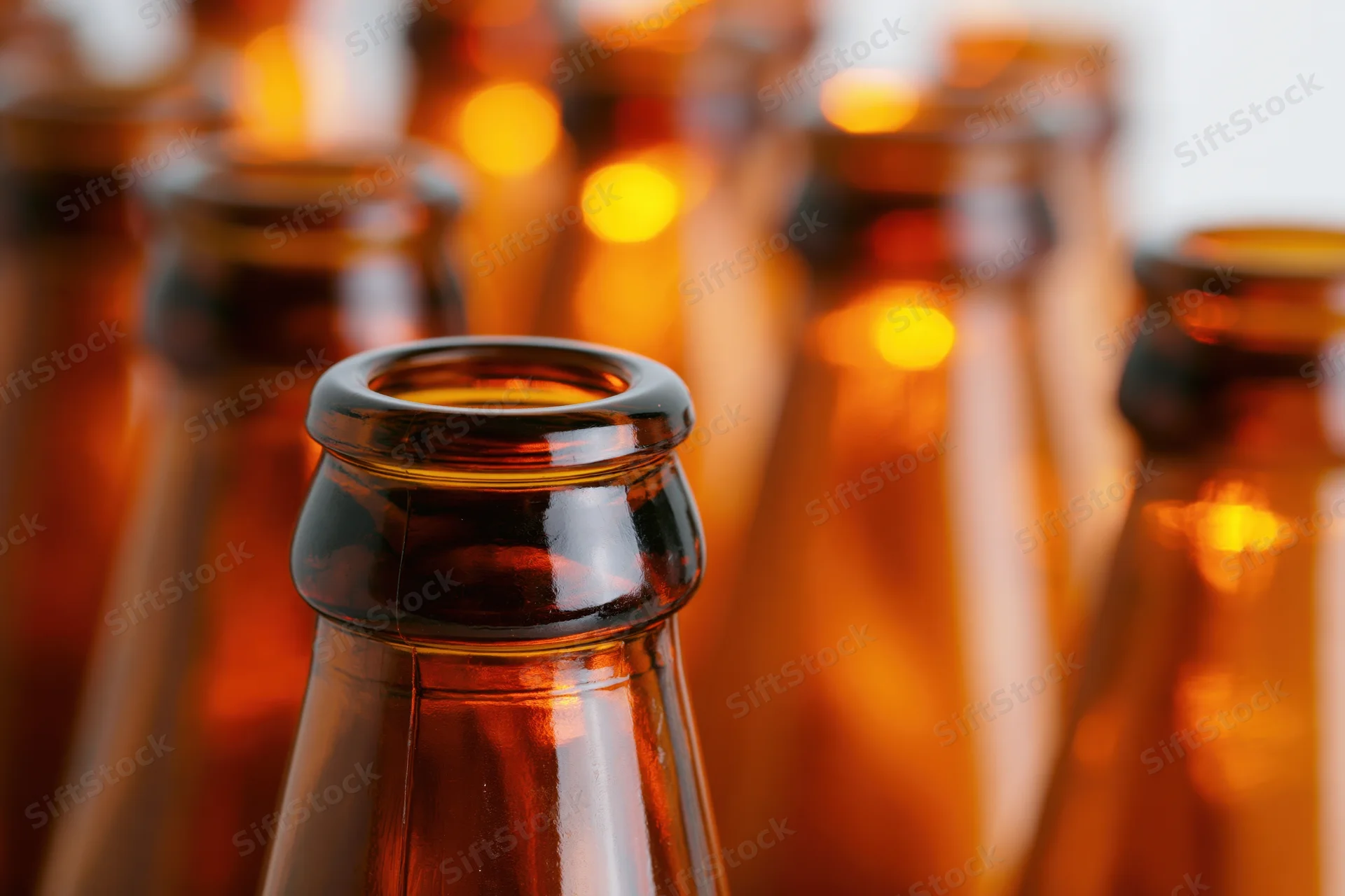 Close-up of empty amber glass beer bottle necks arranged in rows with warm light reflections