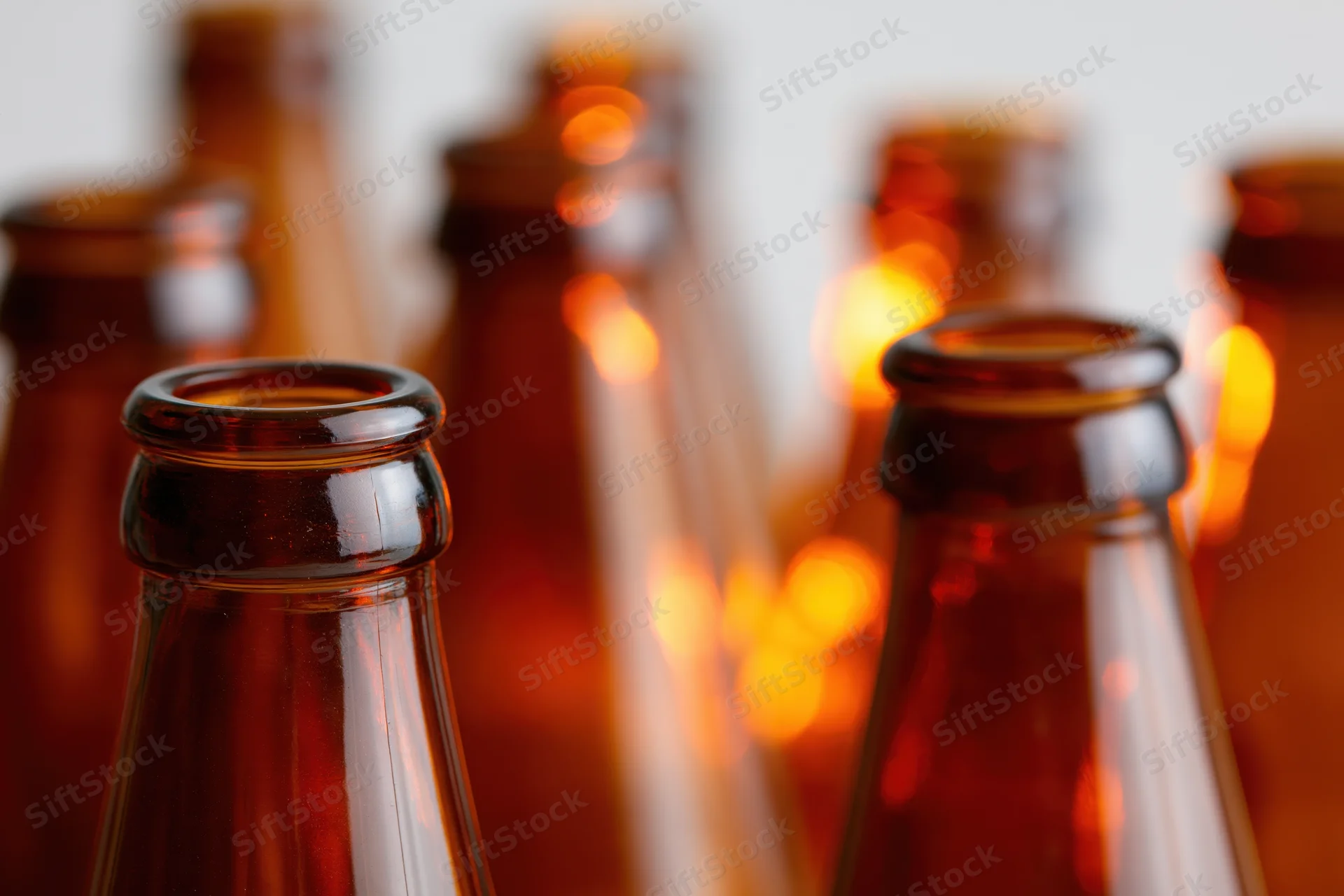 Close-up of empty amber glass beer bottle necks arranged in rows with warm bokeh lighting